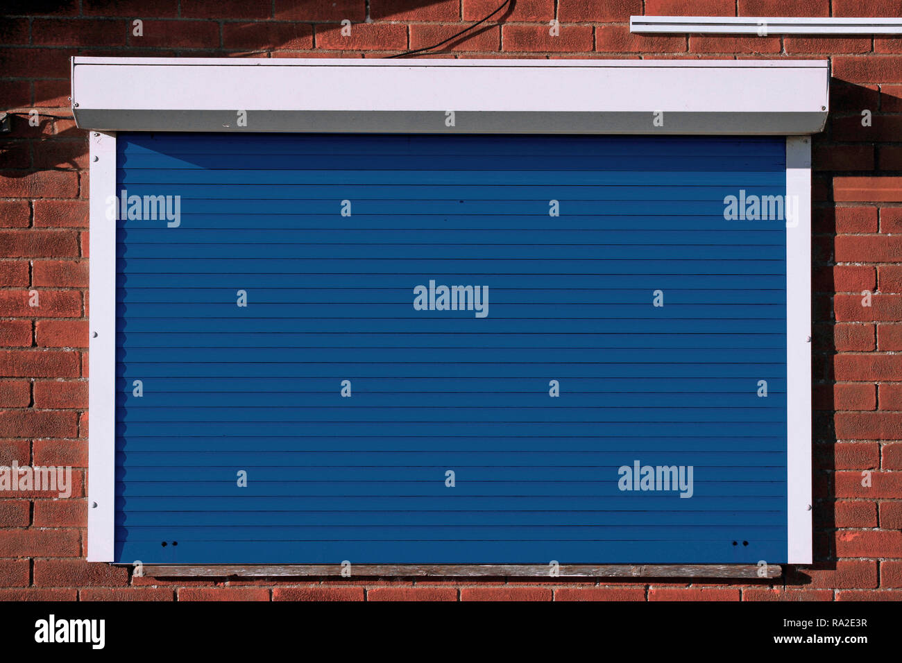 Closed dark blue serving hatch security shutters with brick background Stock Photo