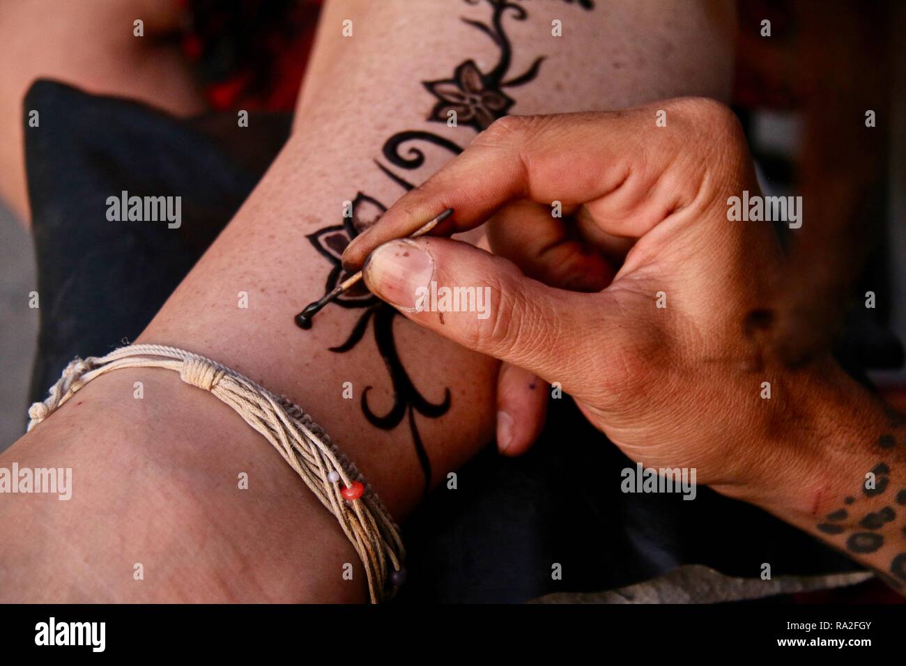 an artist hand freestyle drawing a henna tattoo design up a ladies leg RA2FGY