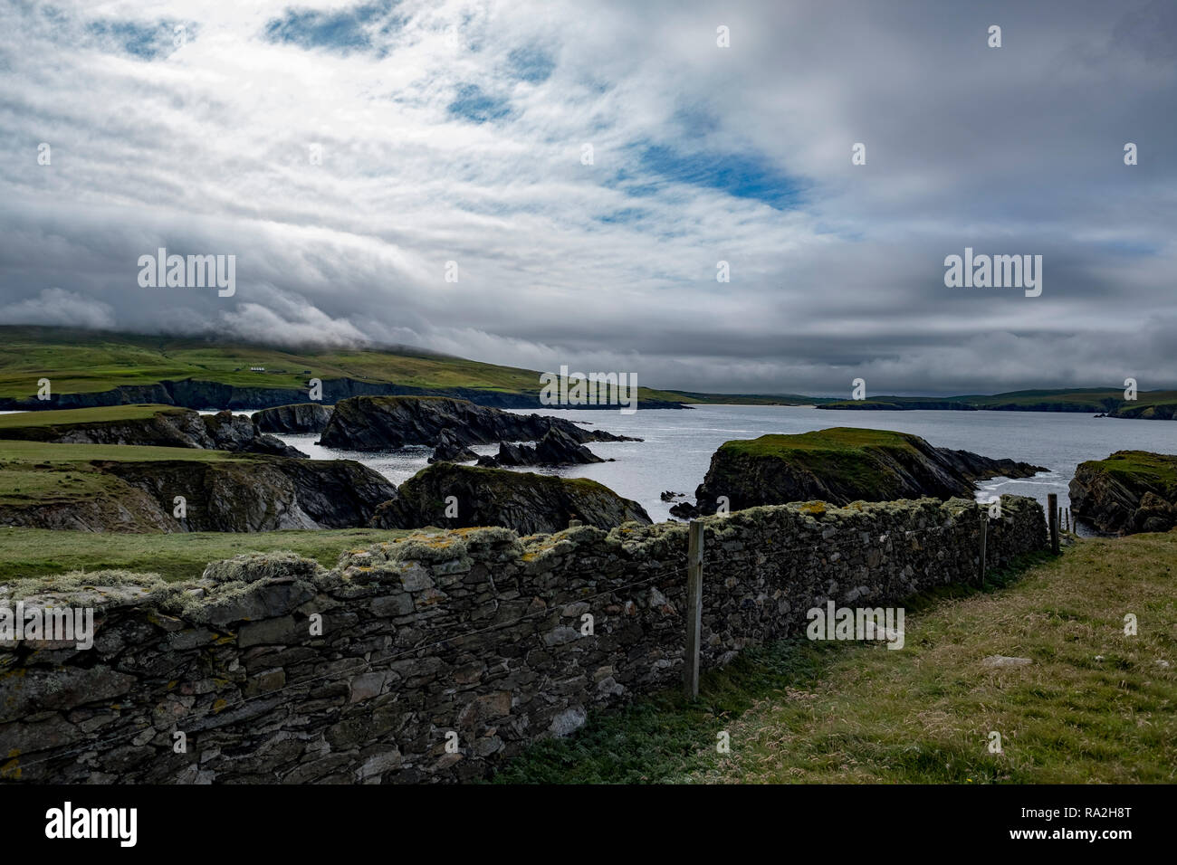 Stone wal separating pasture land on a croft overlooking the Atlantic Ocean on a cloudy day on the Mainland of the Shetland Islands of Scotland Stock Photo