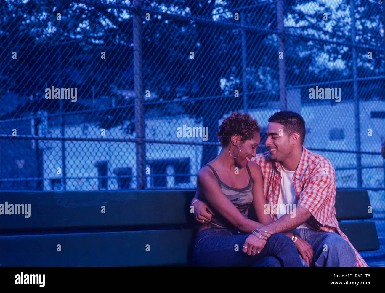 Young Urban ethnic couple flirting on a park bench at dusk or early evening Stock Photo