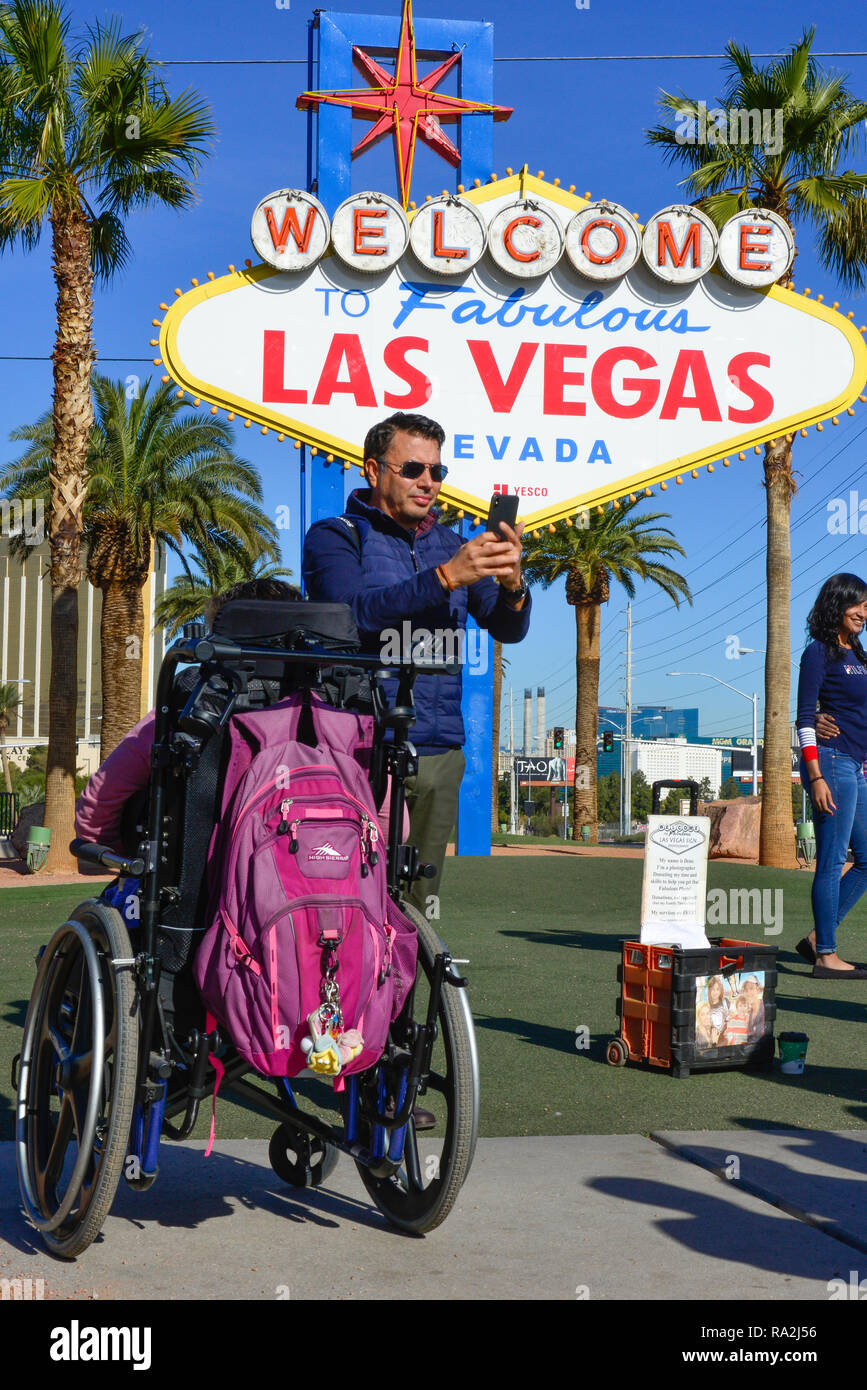 Man with smart phone taking selfie with disabled person in wheelchair in front of famous, vintage, 'Welcome to Fabulous Las Vegas, Nevada' sign Stock Photo