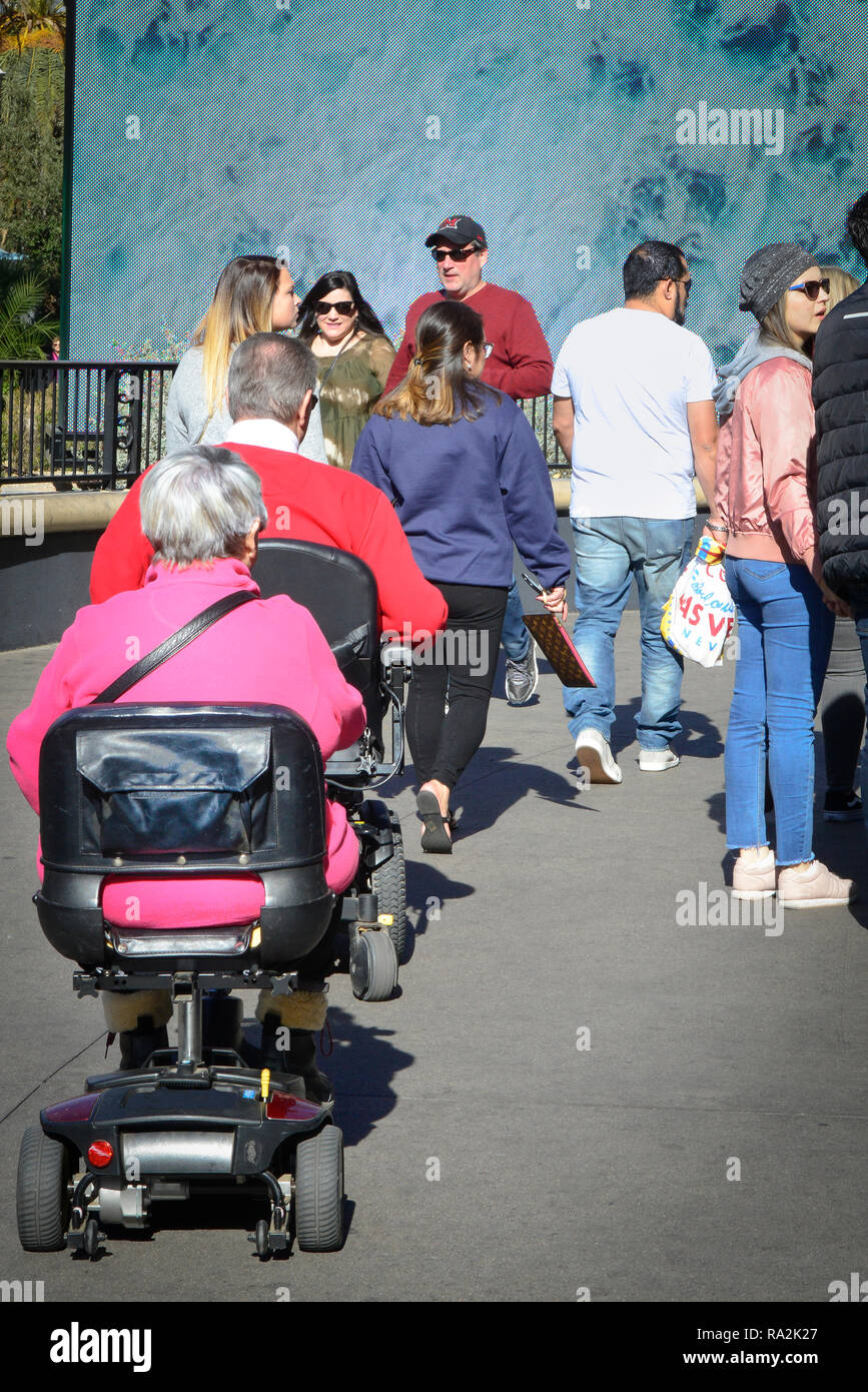 Rear view of A man and a woman, both in wheel chair style scooters joining the crowds on the sidewalk while sightseeing in the USA Stock Photo
