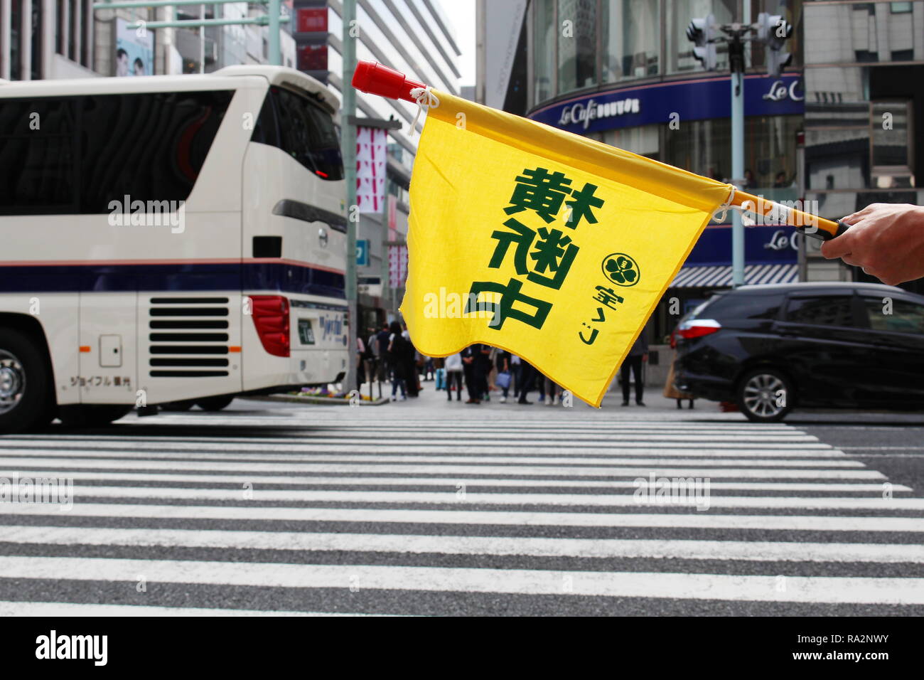 Flag held by crossing guard stationed at a busy crossing in Ginza. 'Crossing' is written on it in Japanese. Sanai Dream Center is in the background. Stock Photo