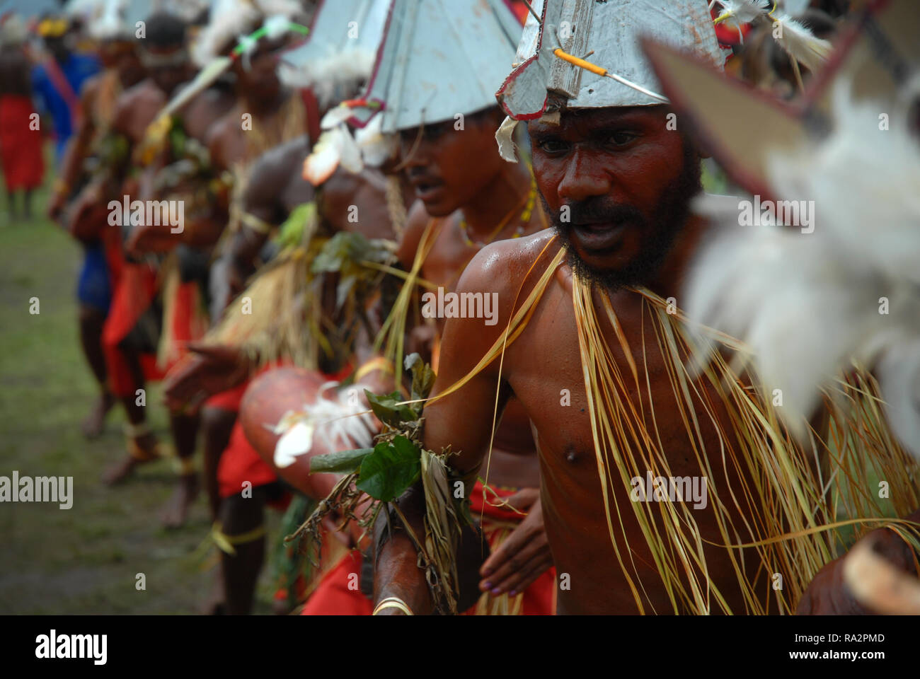 Colourfully dressed and face painted men wearing boat hats dancing as part of a Sing Sing in Madang, Papua New Guinea. Stock Photo