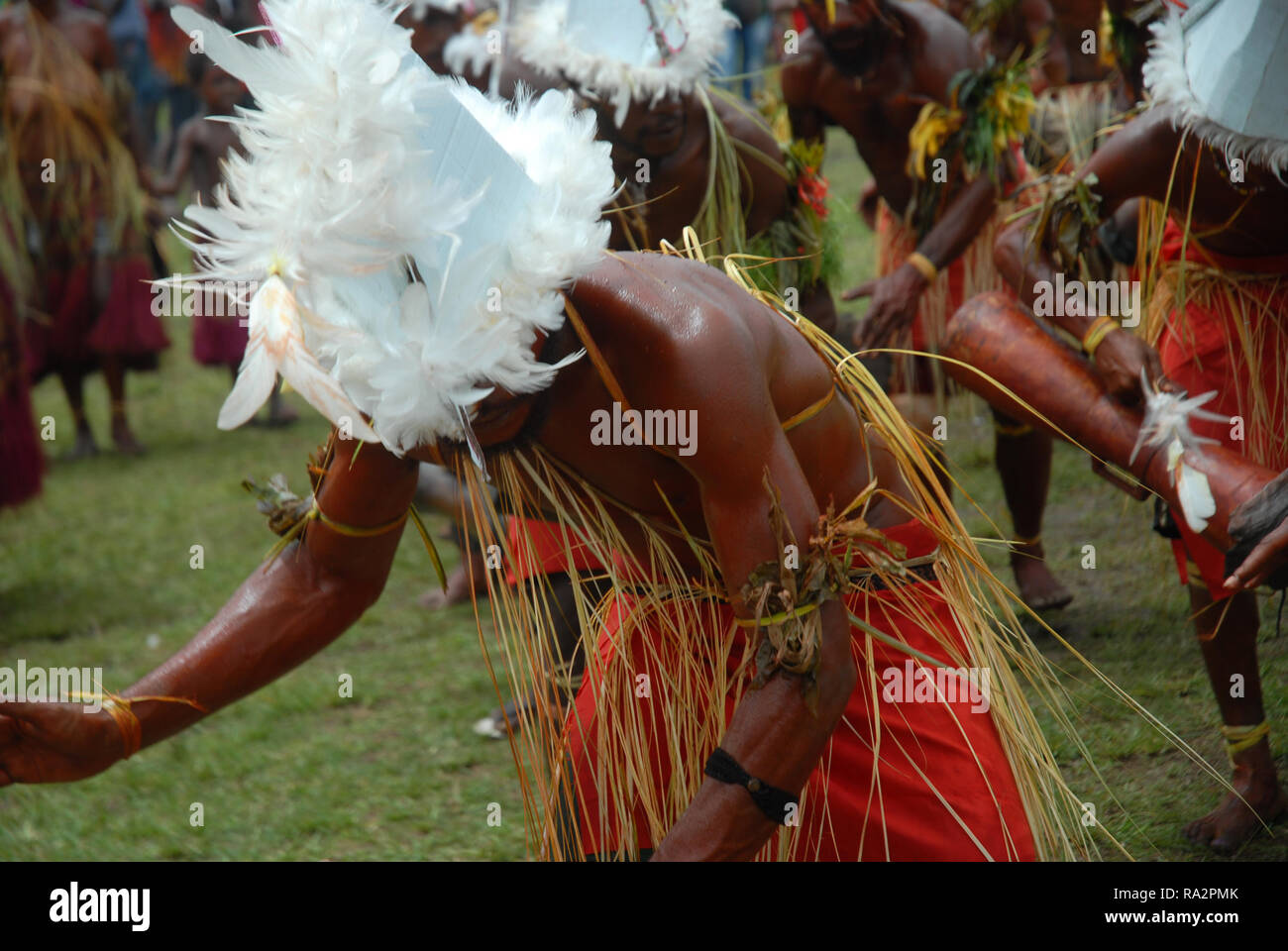Colourfully dressed and face painted men wearing boat hats dancing as part of a Sing Sing in Madang, Papua New Guinea. Stock Photo