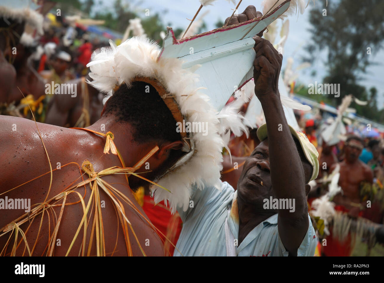 Man putting boat head dress on a colourfully dressed and face painted man as part of the annual Sing Sing in Madang, Papua New Guinea. Stock Photo