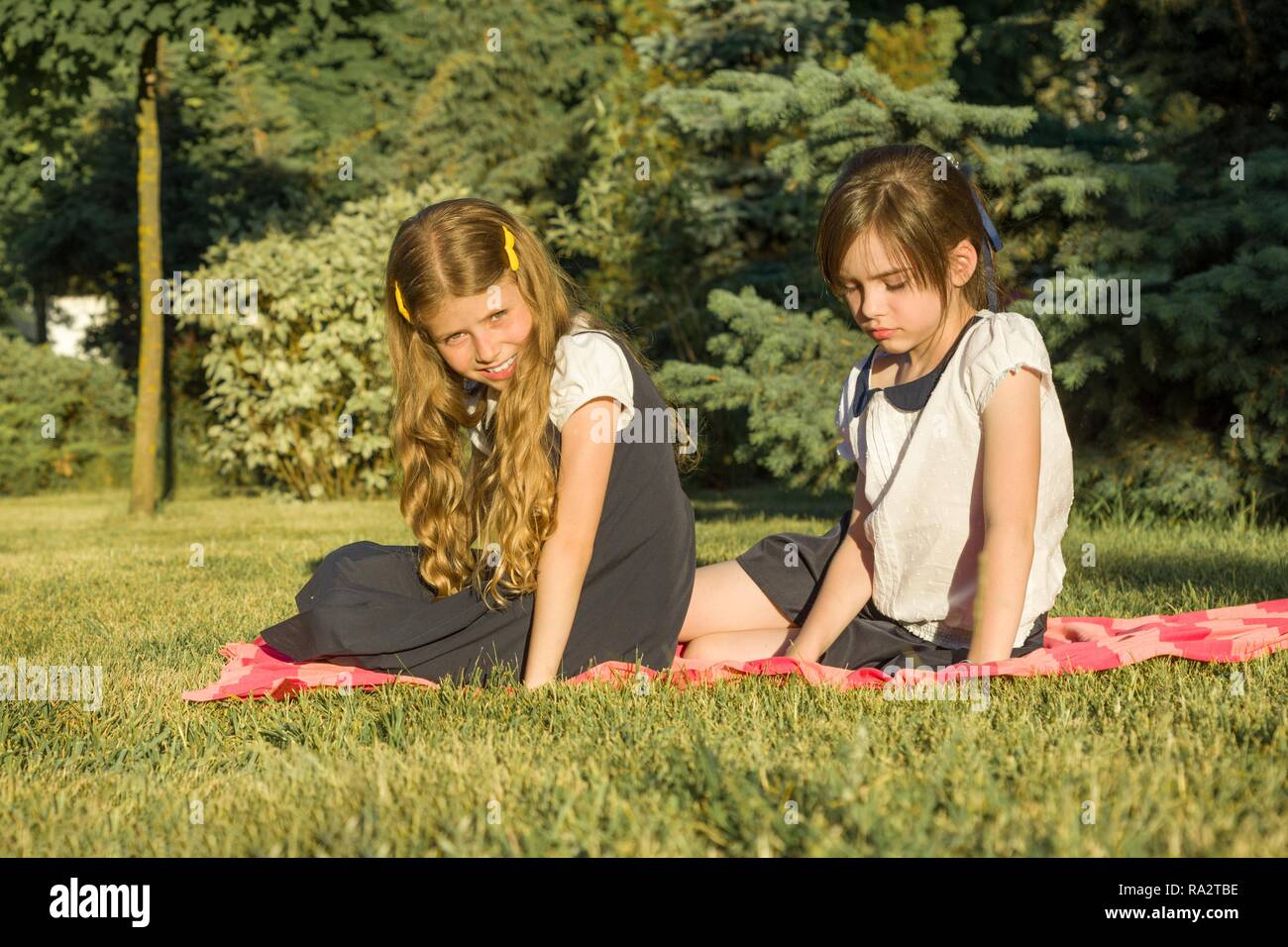 Portrait of two girls friends 7, 8 years old sitting on the grass in the park, golden hour. Stock Photo