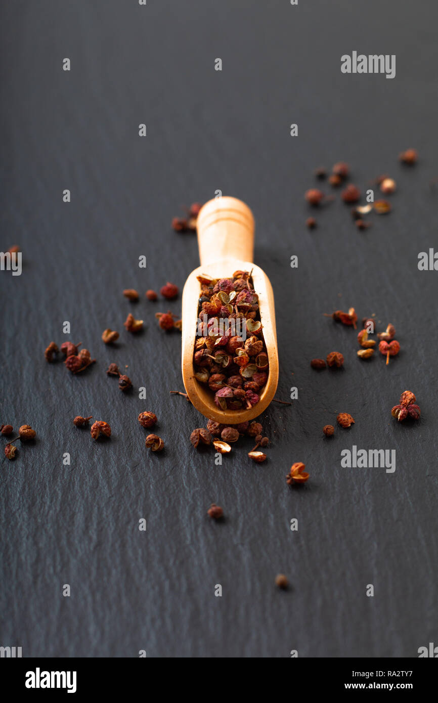 Chinese peppercorn, Sichuan pepper in wooden scoop on black slate stone plate with copy space Stock Photo