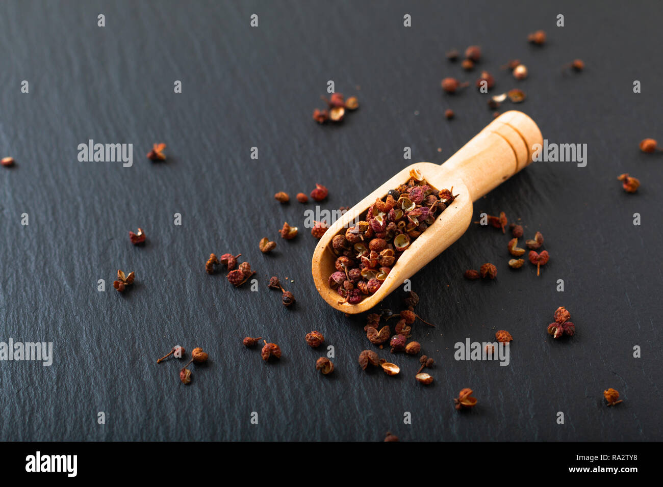 Chinese peppercorn, Sichuan pepper in wooden scoop on black slate stone plate with copy space Stock Photo