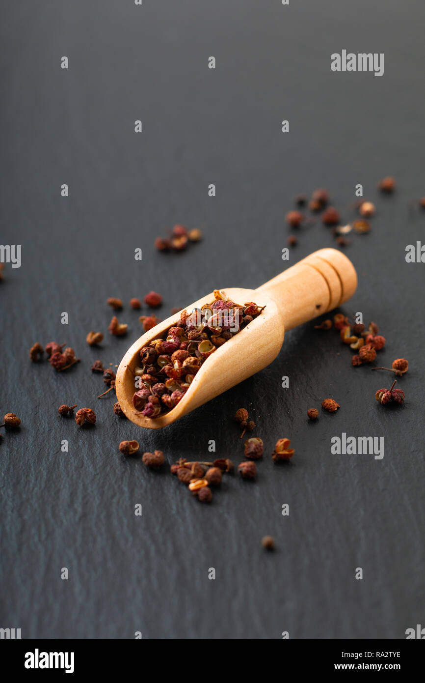 Chinese peppercorn, Sichuan pepper in wooden scoop on black slate stone