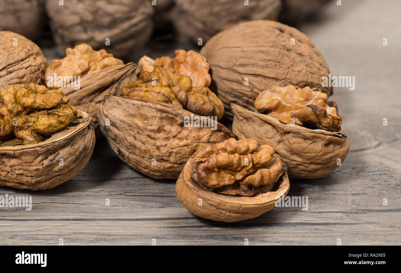 Group of partly peeled nuts with half shells closeup. Cracking of walnuts. Halves of cracked nutshells with nut meat on a wooden background. Walnuts. Stock Photo