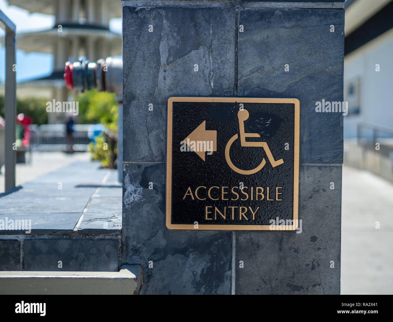 Gold and black accessible entry sign posting with wheelchair handicap logo with arrow pointing to left Stock Photo