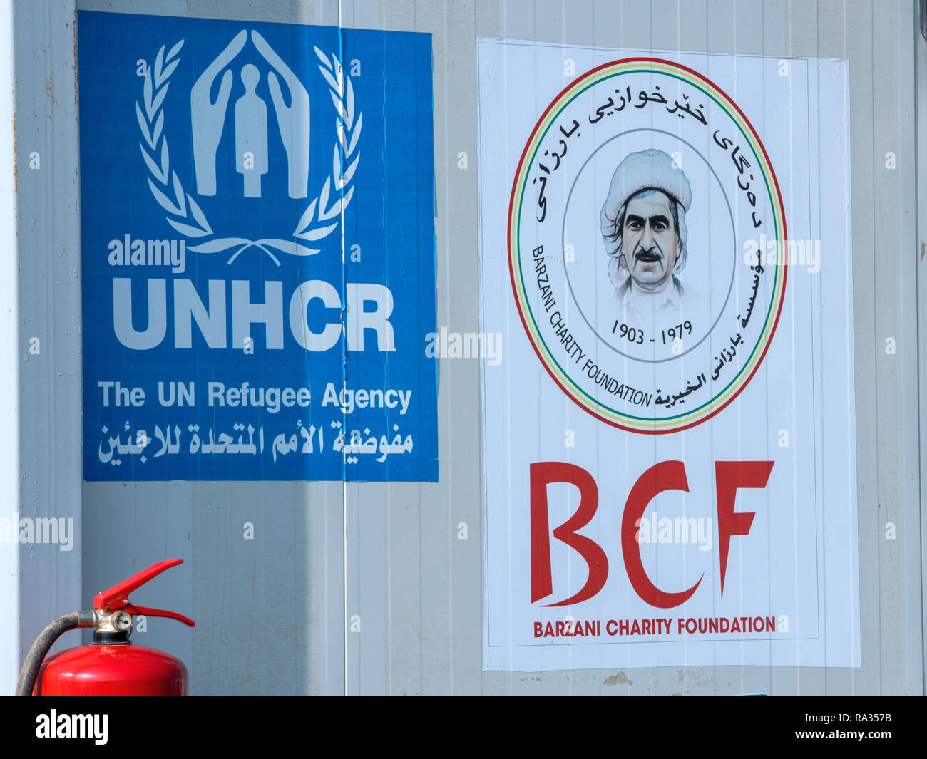Hasan Sham, Iraq. 19th Dec, 2018. The signs of the UN refugee organisation UNHCR and the non-profit organisation Barzani Charity Foundation (BCF), founded in Erbil in 2005, are mounted at the entrance to the refugee camp Hasan Sham at a barrack. The tent camp near the largely destroyed former IS stronghold of Mossul accommodates 3,300 of the 1.8 million internally displaced persons in Iraq. Credit: Jens Büttner/dpa-Zentralbild/ZB/dpa/Alamy Live News Stock Photo
