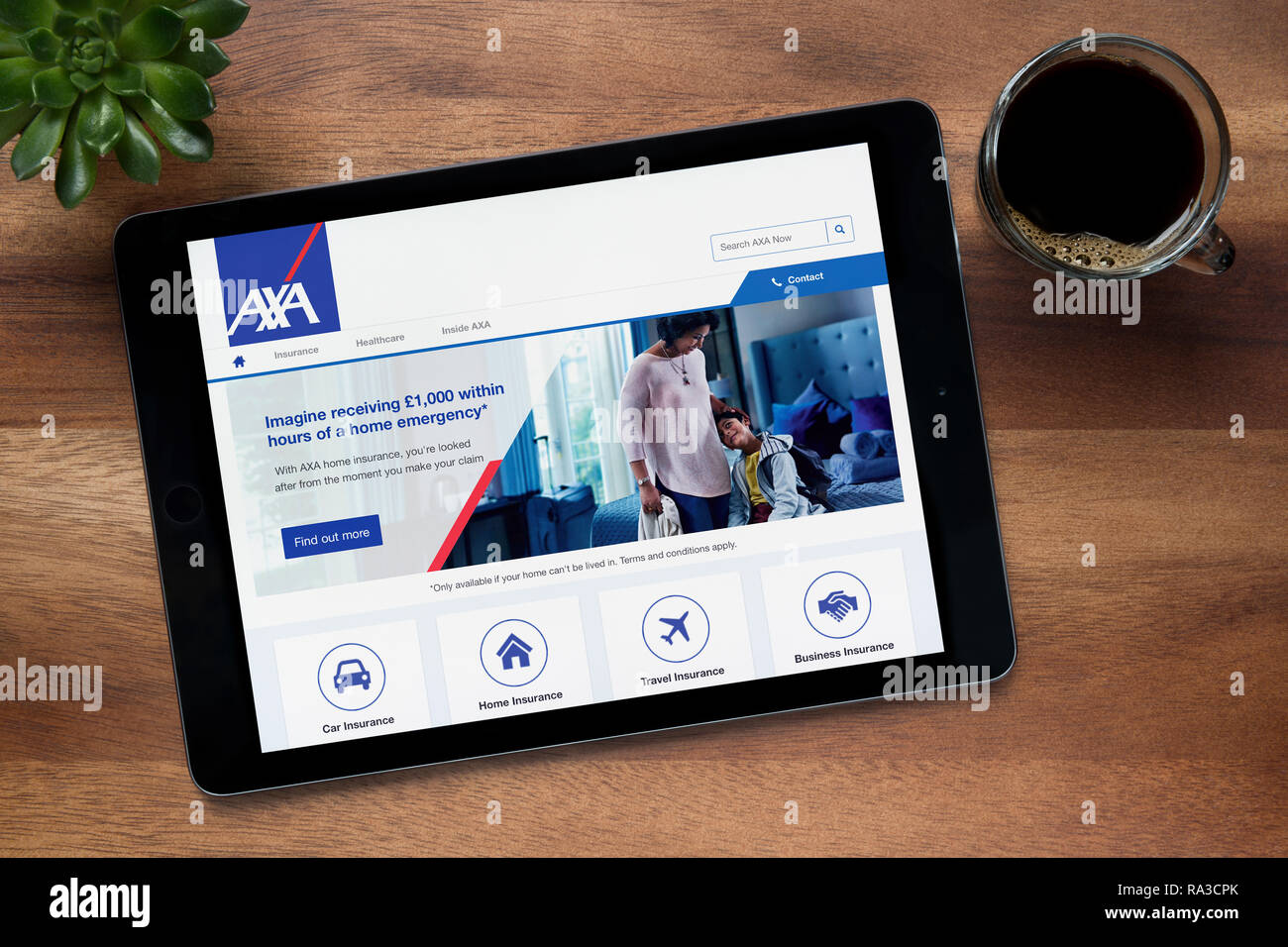 The website of AXA insurance is seen on an iPad tablet, on a wooden table along with an espresso coffee and a house plant (Editorial use only). Stock Photo