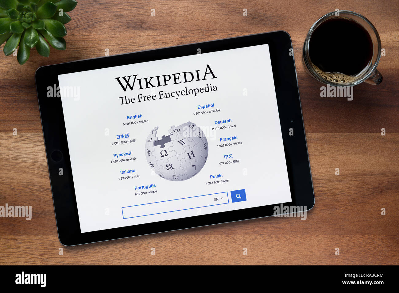 The website of Wikipedia is seen on an iPad tablet, on a wooden table along with an espresso coffee and a house plant (Editorial use only). Stock Photo