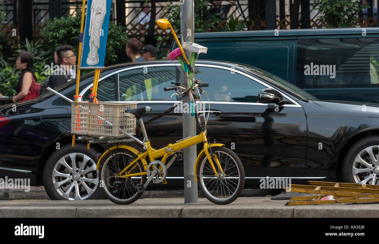 A colourful folding bicycle contrasts with a gleaming black Mercedes Benz in Hong Kong's Lockhart Road Stock Photo