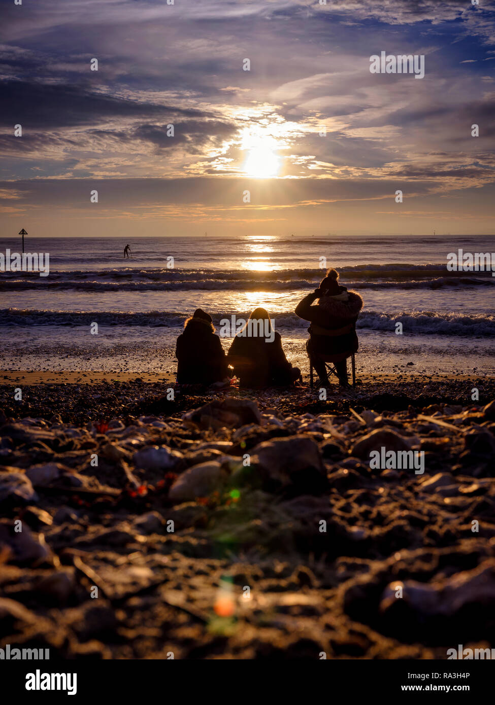 Three people sitting on West Wittering beach wrapped up in winter clothes. Chichester, West Sussex, UK Stock Photo