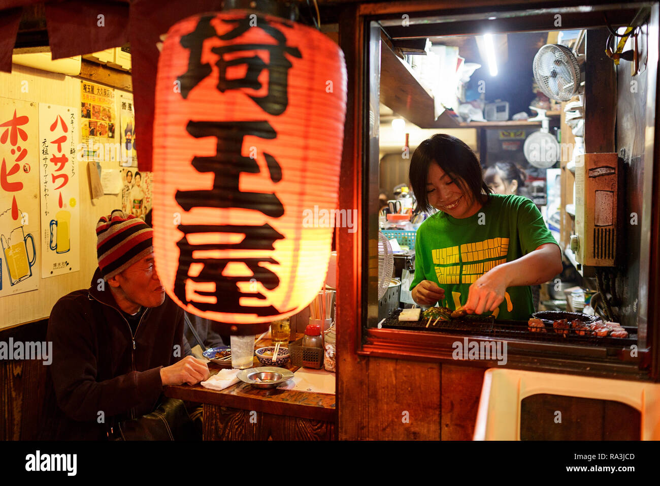 A Japanese chef cooks at Hot and smoky Tokyo street restaurant, as locals eat and drink into the night. Japan Stock Photo