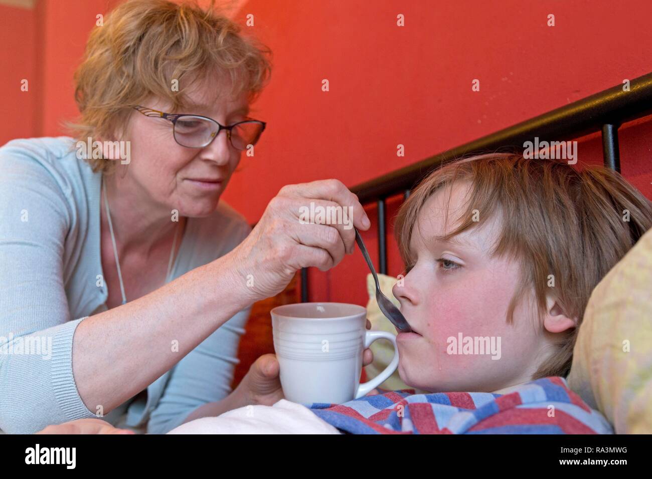 Mother takes care of sick son in bed, symbol picture, cold, care, parents, childhood, Germany Stock Photo