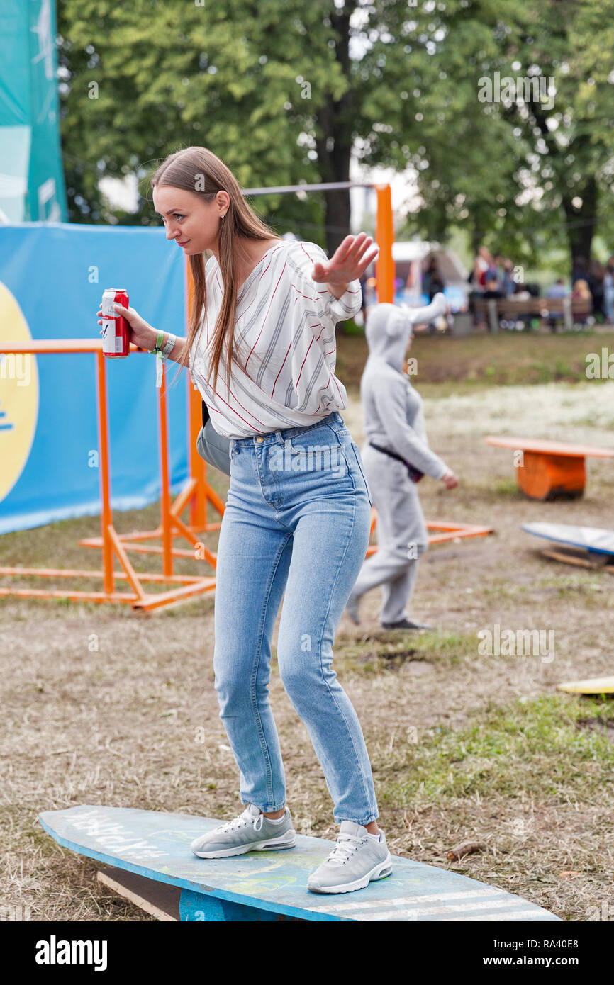 KIEV, UKRAINE - JULY 04, 2018: Young beautiful smiling woman with Budweiser beer dressed in summer clothes have a fun on wooden wakeboard outdoor at t Stock Photo