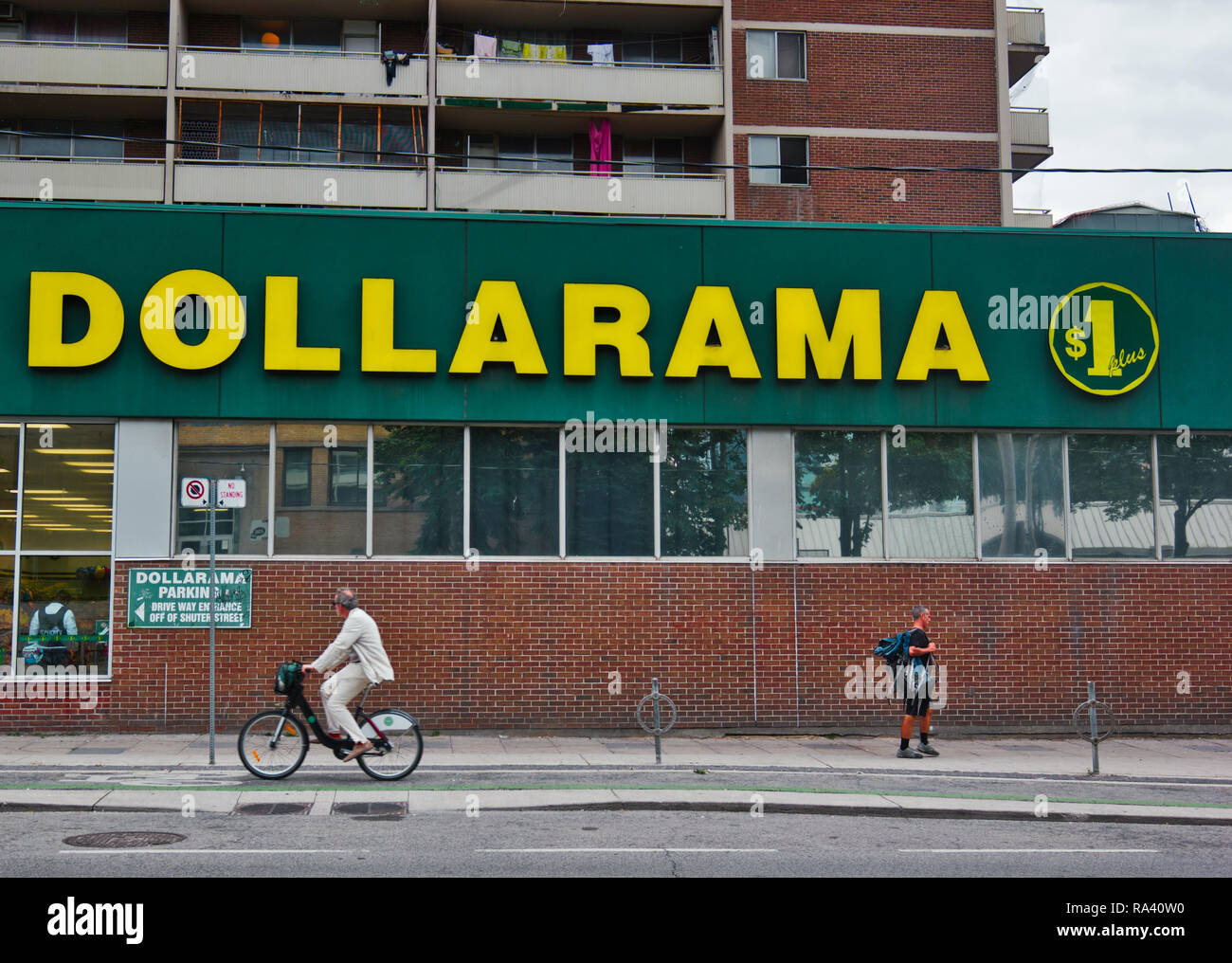 Cyclist and pedestrian passing a Dollarama dollar retail store, Toronto, Ontario, Canada Stock Photo