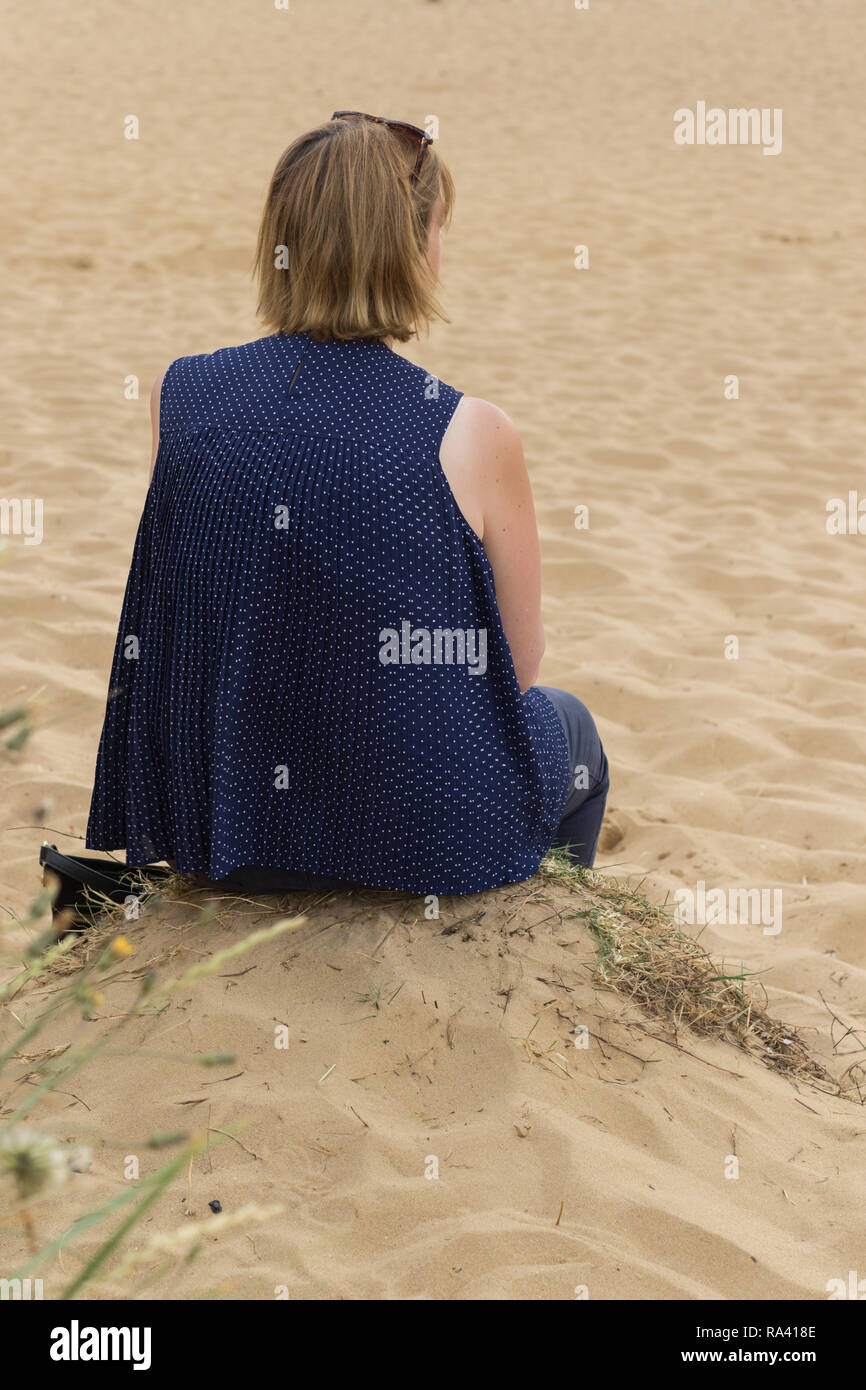 Woman sitting on the beach looking out to sea alone.England, UK Stock ...