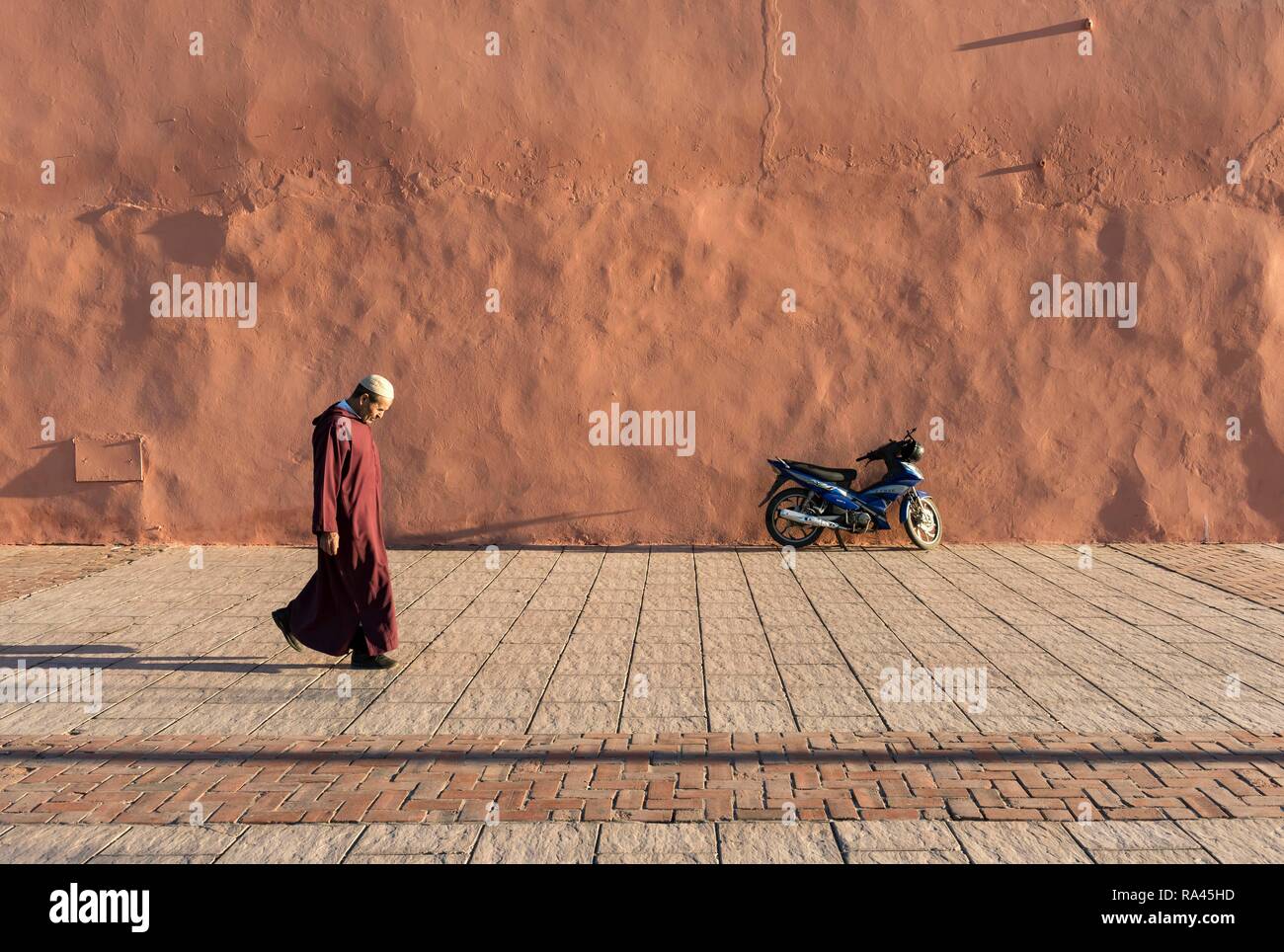 Man walks along red-orange city walls of Marrakech, Morocco Stock Photo