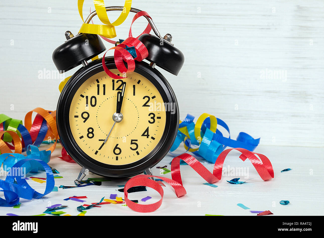 midnight time on retro black clock for New Years Eve party with colorful ribbon and confetti on whitewashed wood Stock Photo