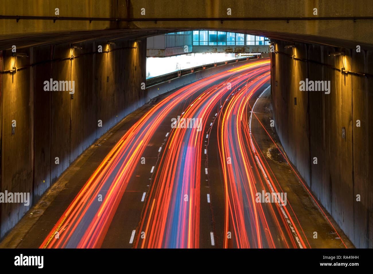 Long exposure of a motorway traffic at night - light trails painted in the shot with a subway station in the background. Stock Photo
