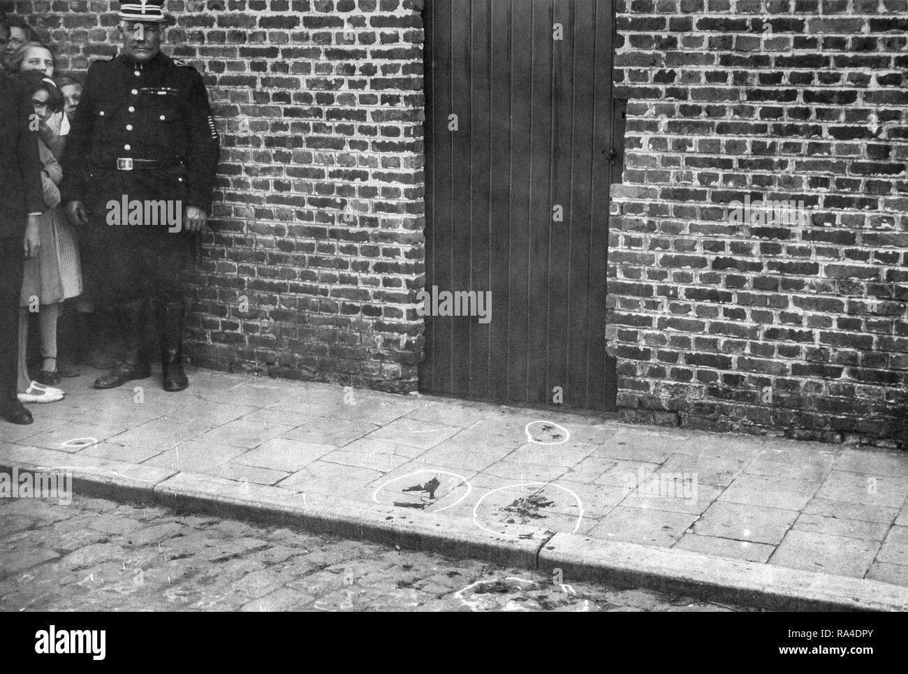 Mid twentieth century black and white photo showing police officer / gendarme and marked blood stains at crime scene on pavement Stock Photo