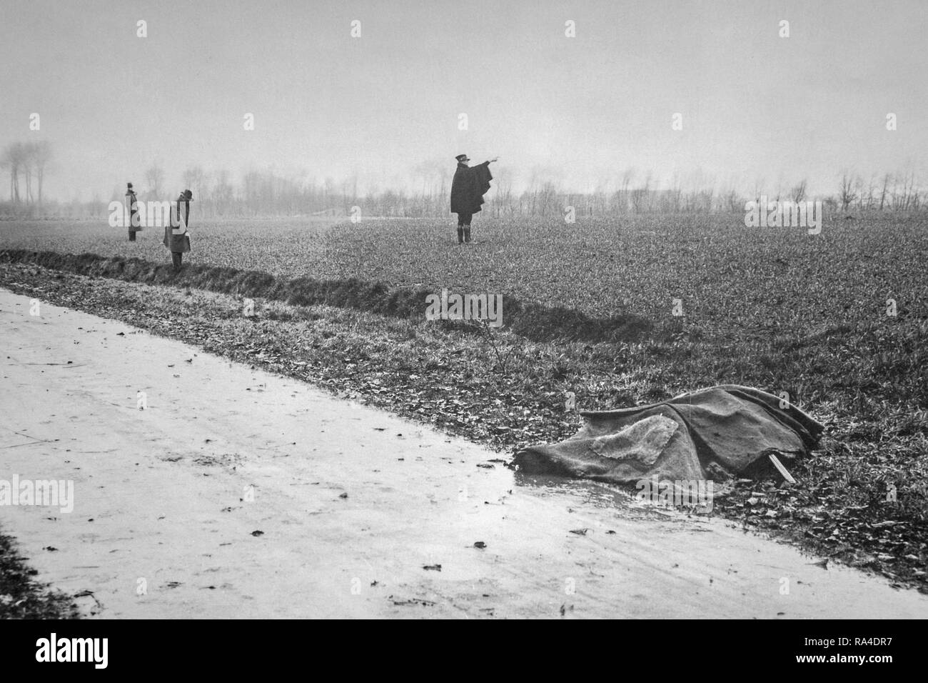 Mid twentieth century black and white photo showing murdered victim covered with cloth and gendarme and police inspectors inspecting field and ditch Stock Photo