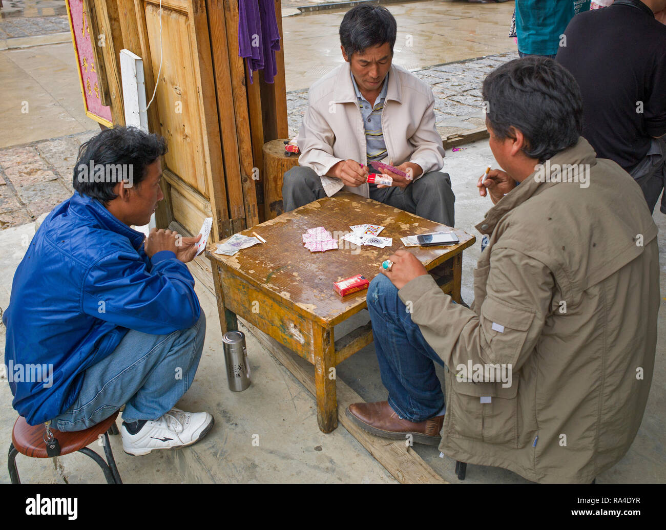 Three Chinese men sitting playing cards while sitting on stools in shop ...