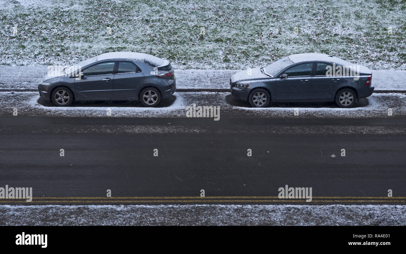 Two grey cars parked in suburban road during snow shower with light covering of snow parked, Sheffield, UK Stock Photo