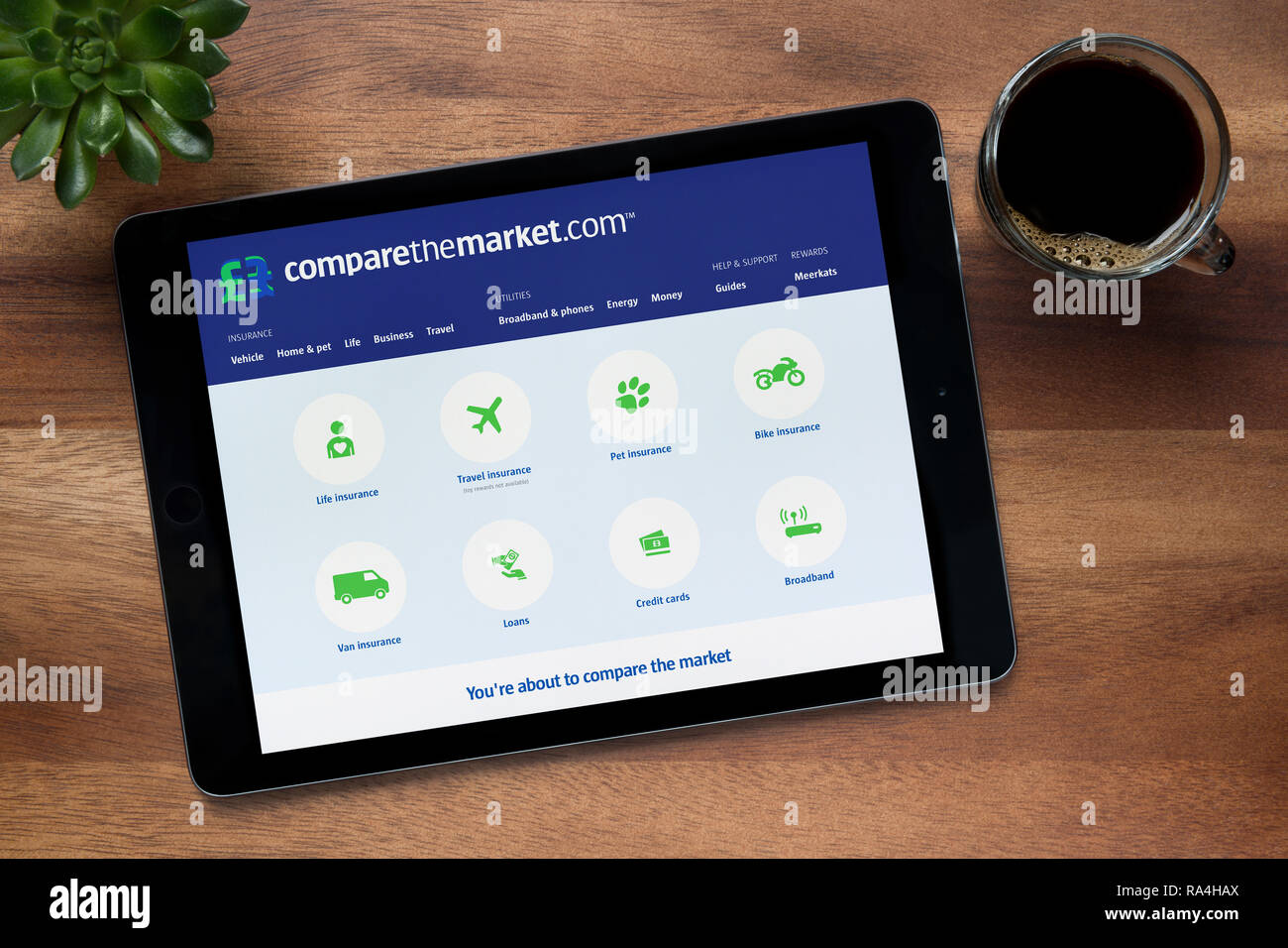 The website of Compare The Market is seen on an iPad tablet, on a wooden table along with an espresso coffee and a house plant (Editorial use only). Stock Photo