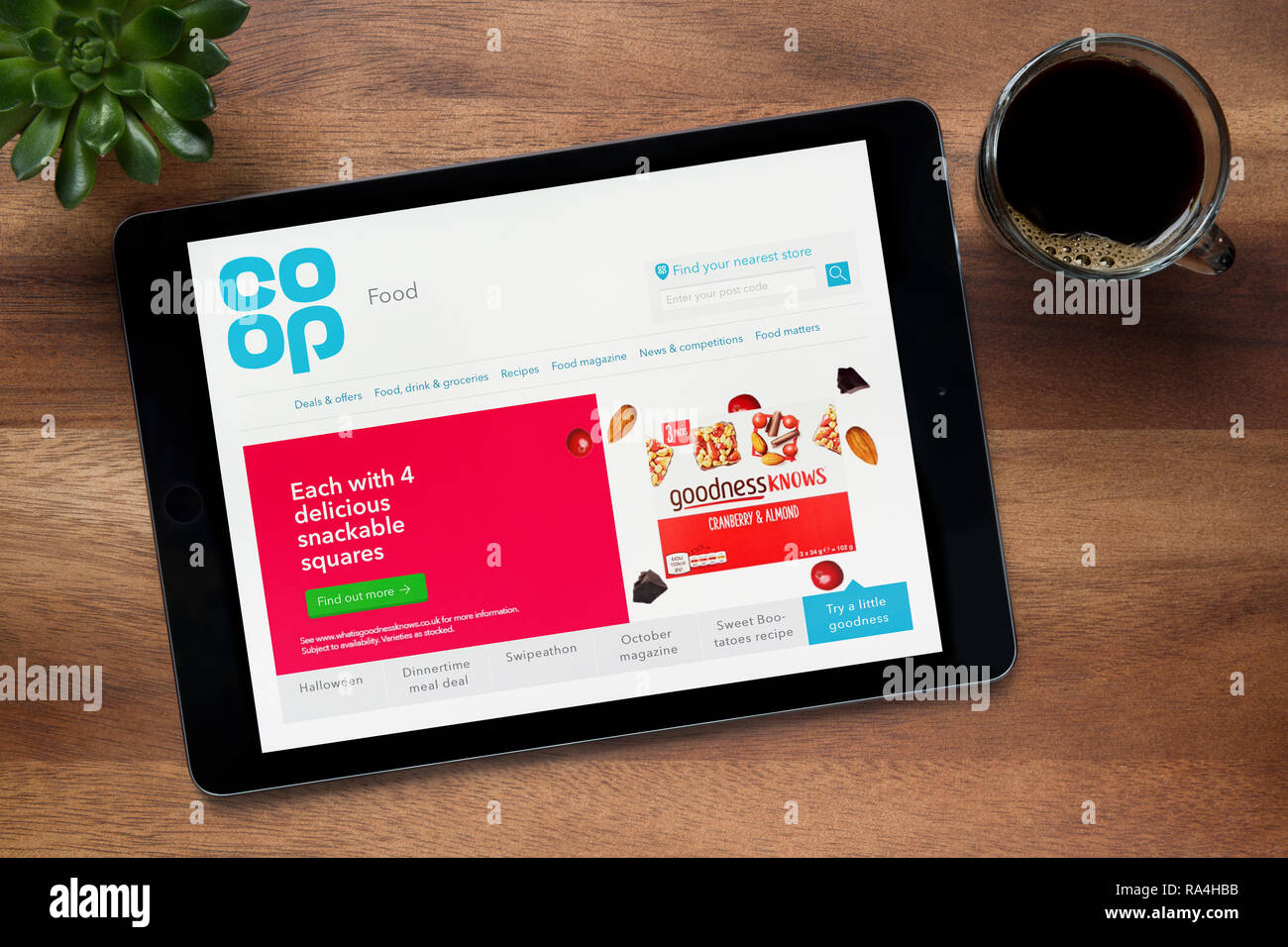 The website of Co-op food is seen on an iPad tablet, on a wooden table along with an espresso coffee and a house plant (Editorial use only). Stock Photo