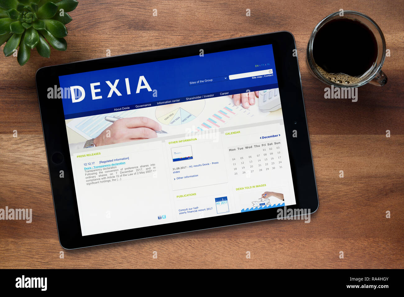 The website of Dexia Group is seen on an iPad tablet, on a wooden table along with an espresso coffee and a house plant (Editorial use only). Stock Photo