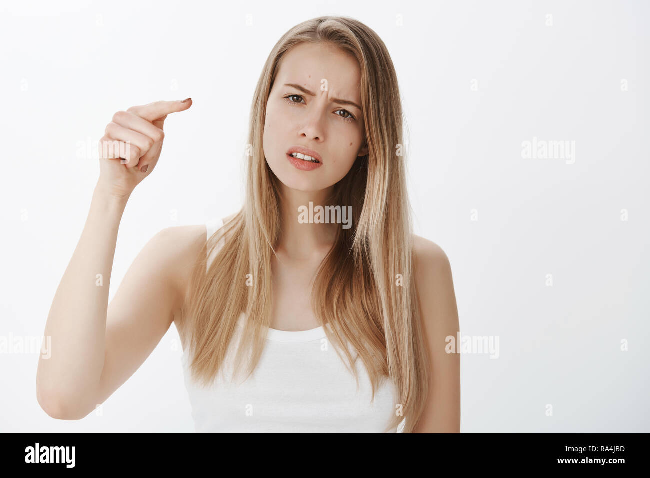 Girl blaming friend for hurting her feelings, being offended and hurt, pointing at camera as accusing someone frowning and squinting, sad as mate let her down standing gloomy over gray background Stock Photo