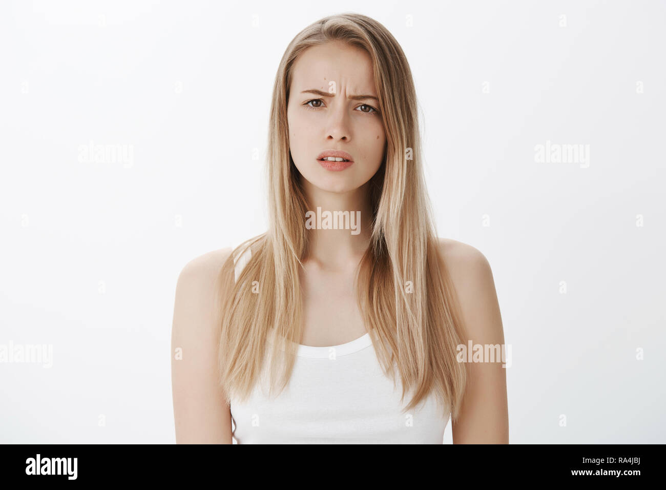 Portrait of confused puzzled attractive european female model with blond hair frowning and squinting as cannot get clue, standing questioned and clueless against gray background Stock Photo