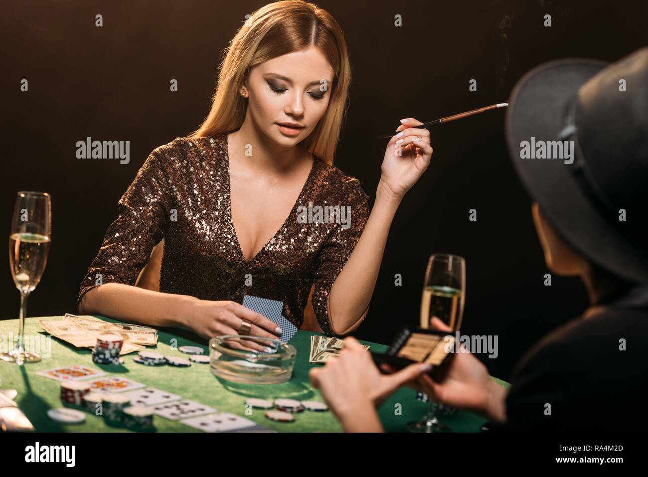 attractive girls smoking cigarettes and playing poker at table in
