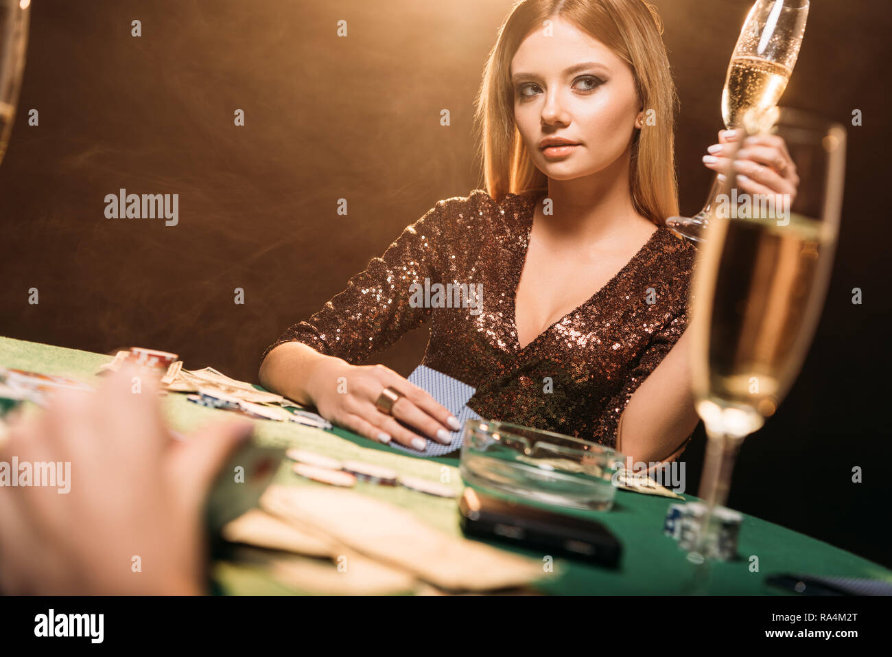 attractive girl holding glass of champagne at poker table in ...