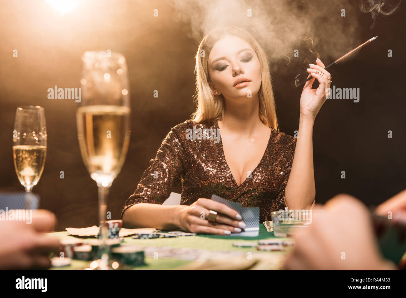 selective focus of attractive girl smoking cigarette at poker table in casino Stock Photo