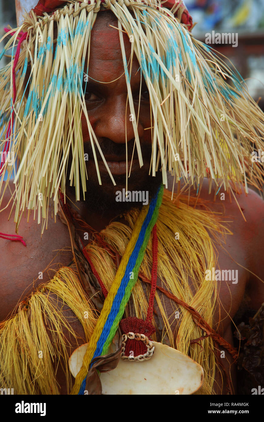 Colourfully dressed and face painted man wearing a straw hat dancing as part of a Sing Sing in Madang, Papua New Guinea. Stock Photo
