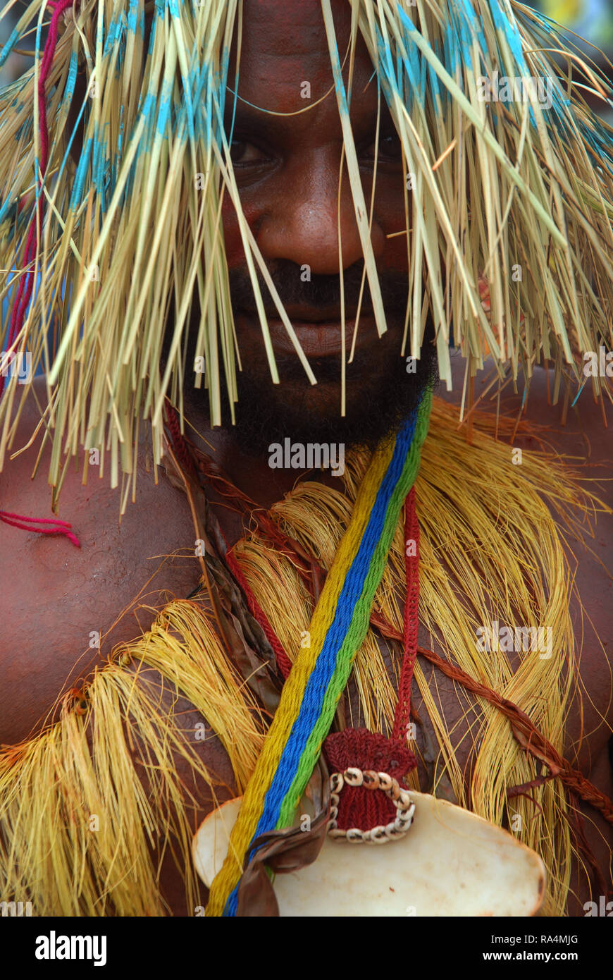 Colourfully dressed and face painted man wearing a straw hat dancing as part of a Sing Sing in Madang, Papua New Guinea. Stock Photo