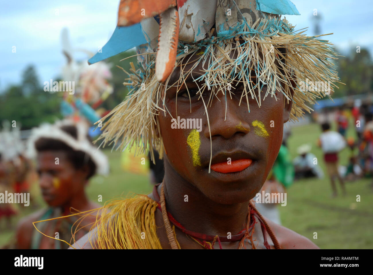 Colourfully dressed and face painted man wearing a straw hat as part of a Sing Sing in Madang, Papua New Guinea. Stock Photo