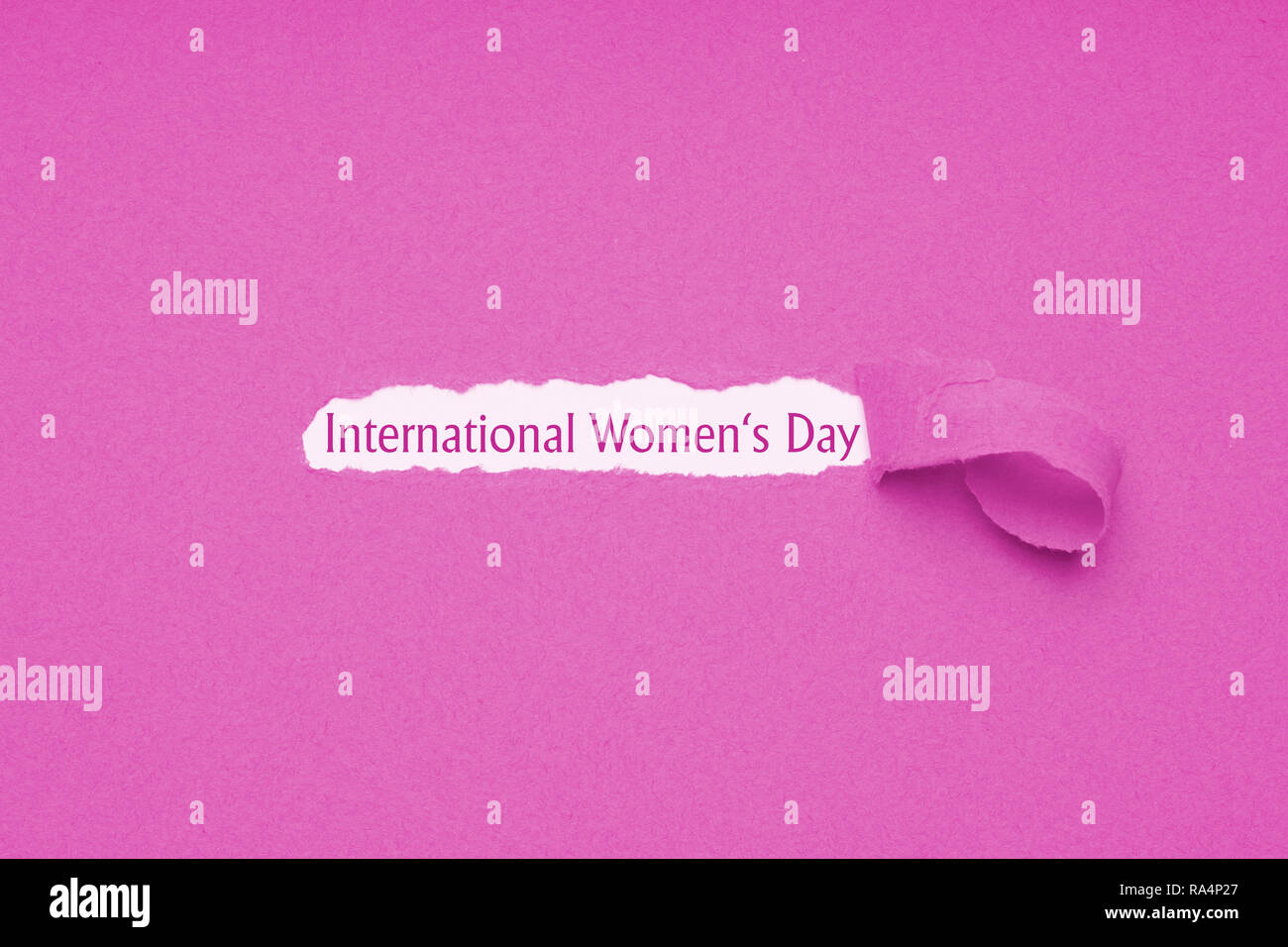 International womens day is celebrated on March 8 - text revealed by hole torn in pink paper background Stock Photo