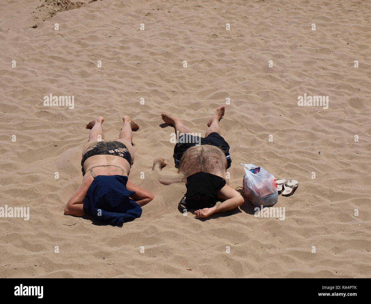 Man and woman buried in sand and covering faces whilst sun bathing in Altinkum Turkey Stock Photo