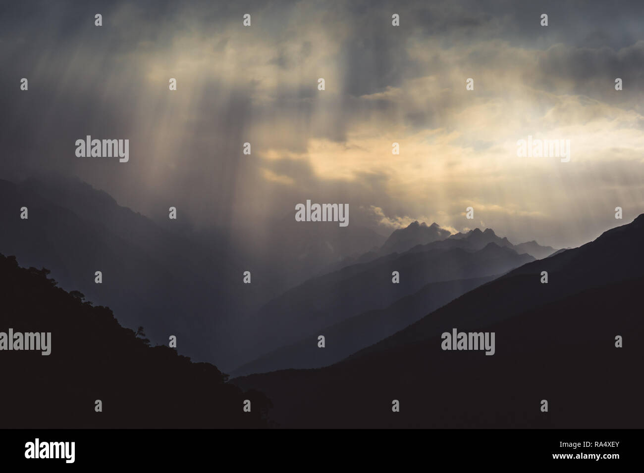 Beams of sunlight shiny through grey clouds over a rugged mountain range in a moody wilderness landscape Stock Photo
