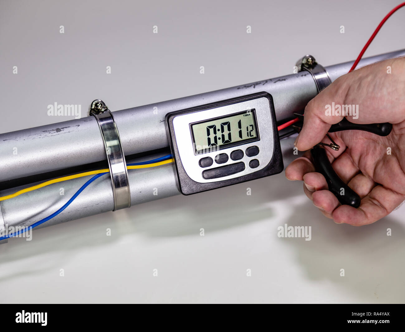 Hand cutting wire on pipe bomb with an lcd clock timer to trigger detonation on white background Stock Photo