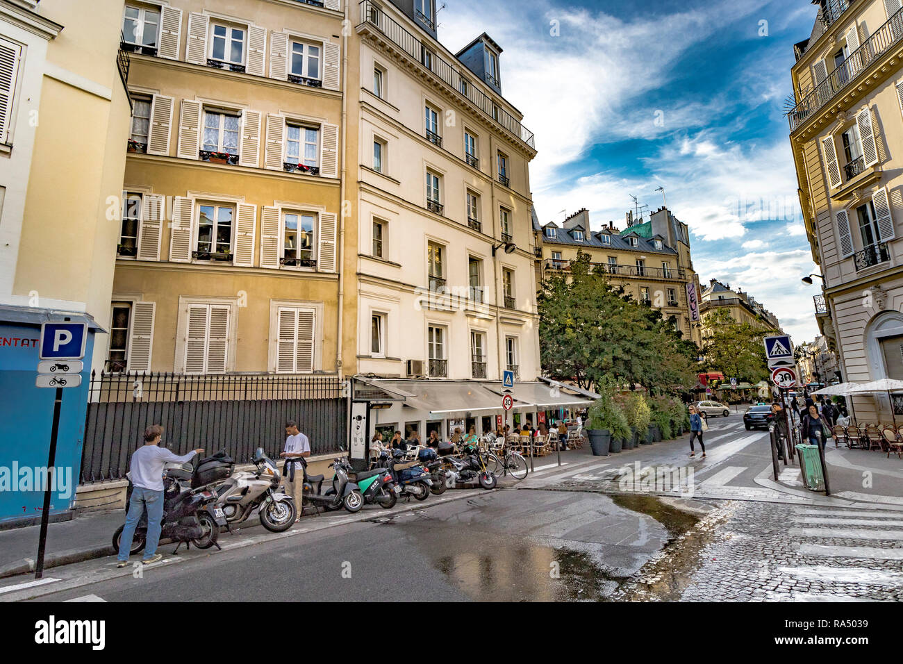 A man parks a Motor scooter near a busy restaurant whilst another man looks at his phone, along Rue de Douai,in ThePigalle area of Paris Stock Photo