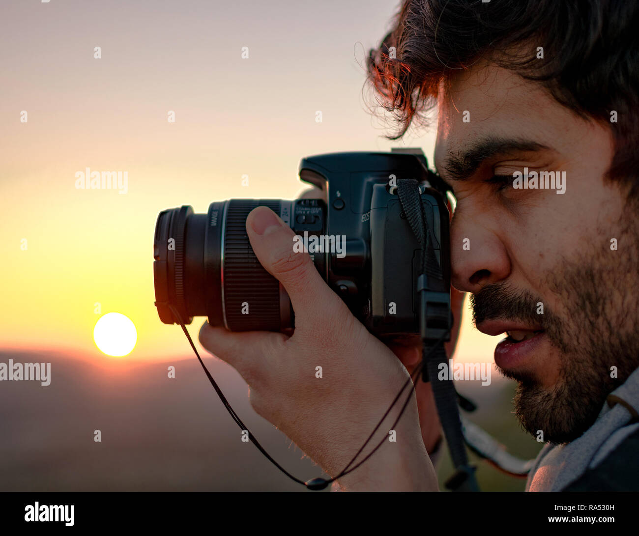 Portrait of man taking photos with camera reflex against sunset.Winter outdoor activities. Spanish, latin photographers at mountain top in Spain, 2019. Stock Photo